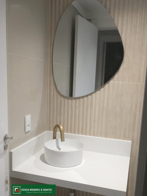 Lavabo com bancada clara, cuba de apoio redonda e torneira dourada